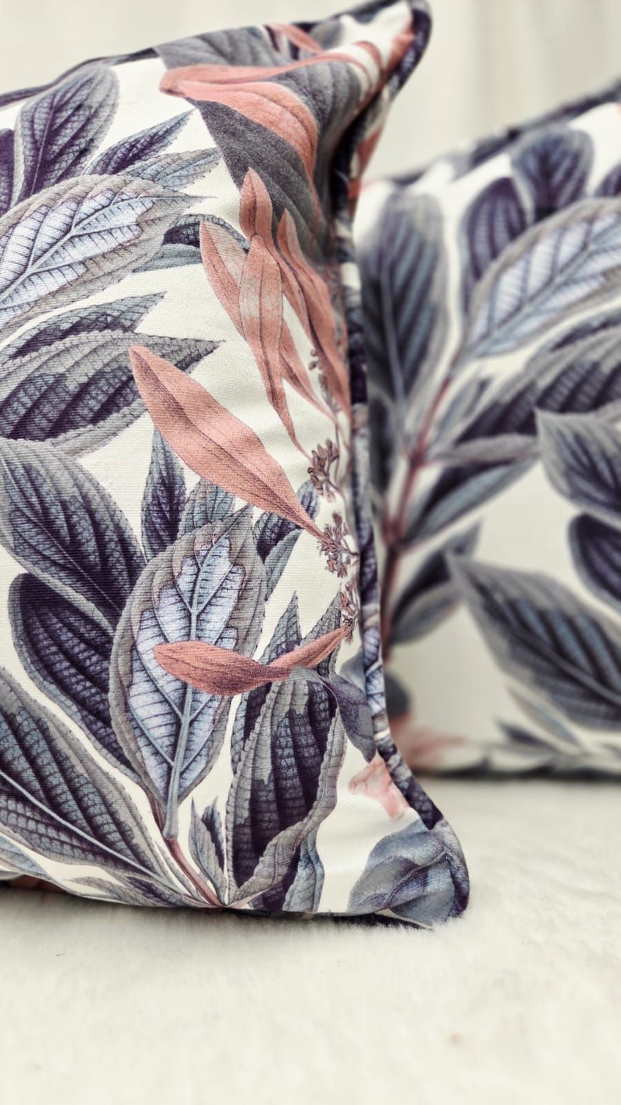 Two decorative throw pillows with botanical leaf print in muted purple, grey, and blush pink tones on white fabric.