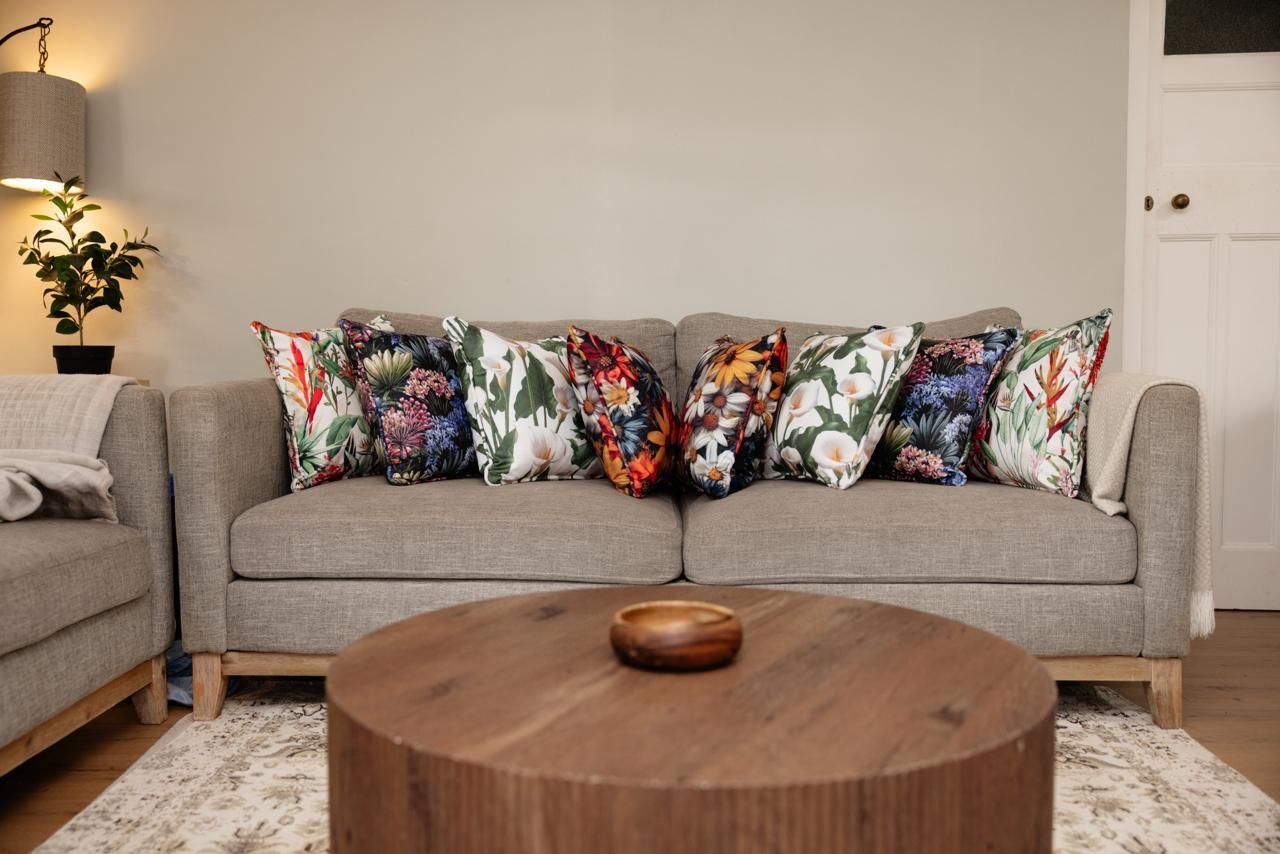 Gray sofa with colorful floral throw pillows in a modern living room with a round wooden coffee table.