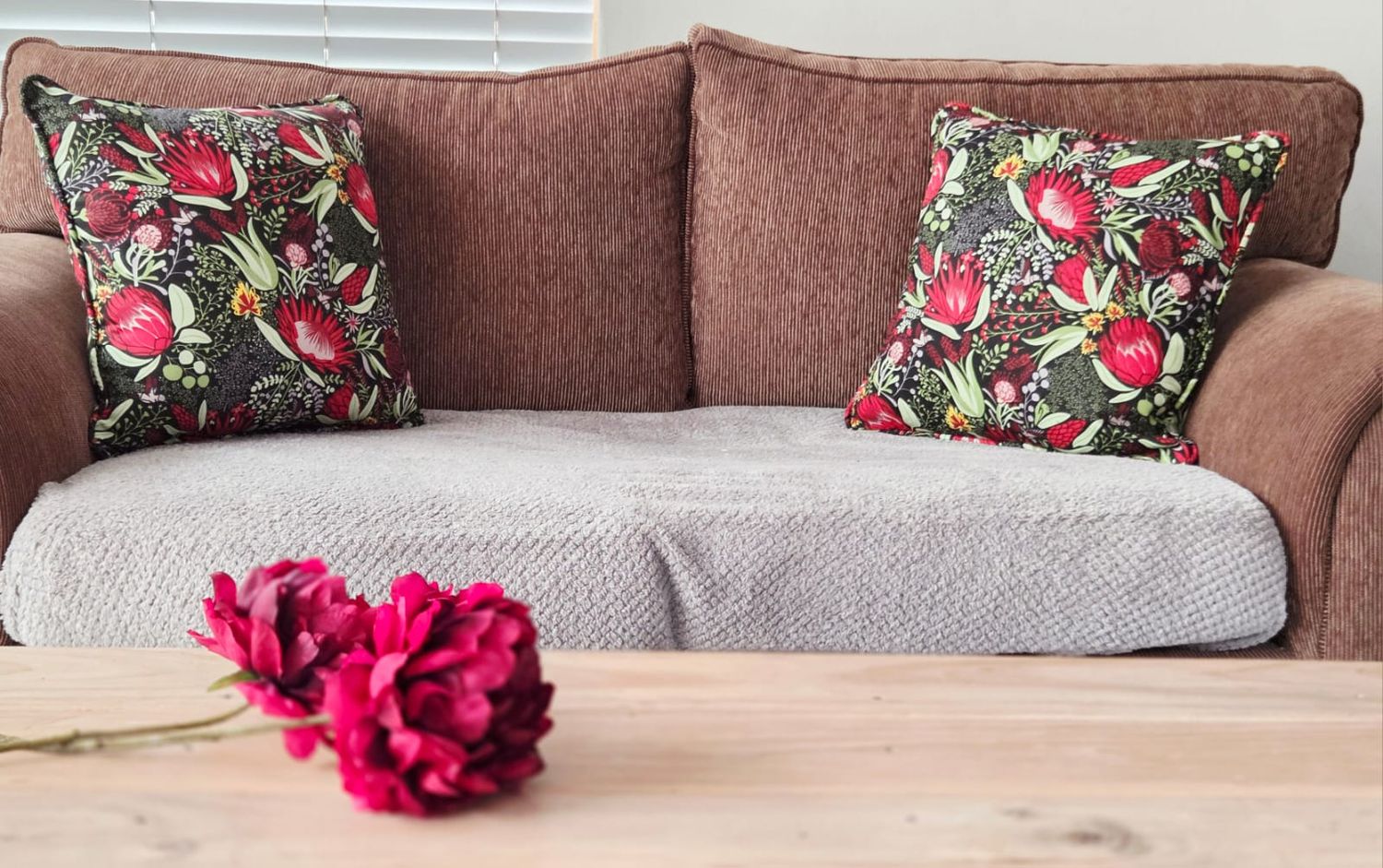 Brown sofa with floral throw pillows and a wooden coffee table with pink peonies in a cozy living room.