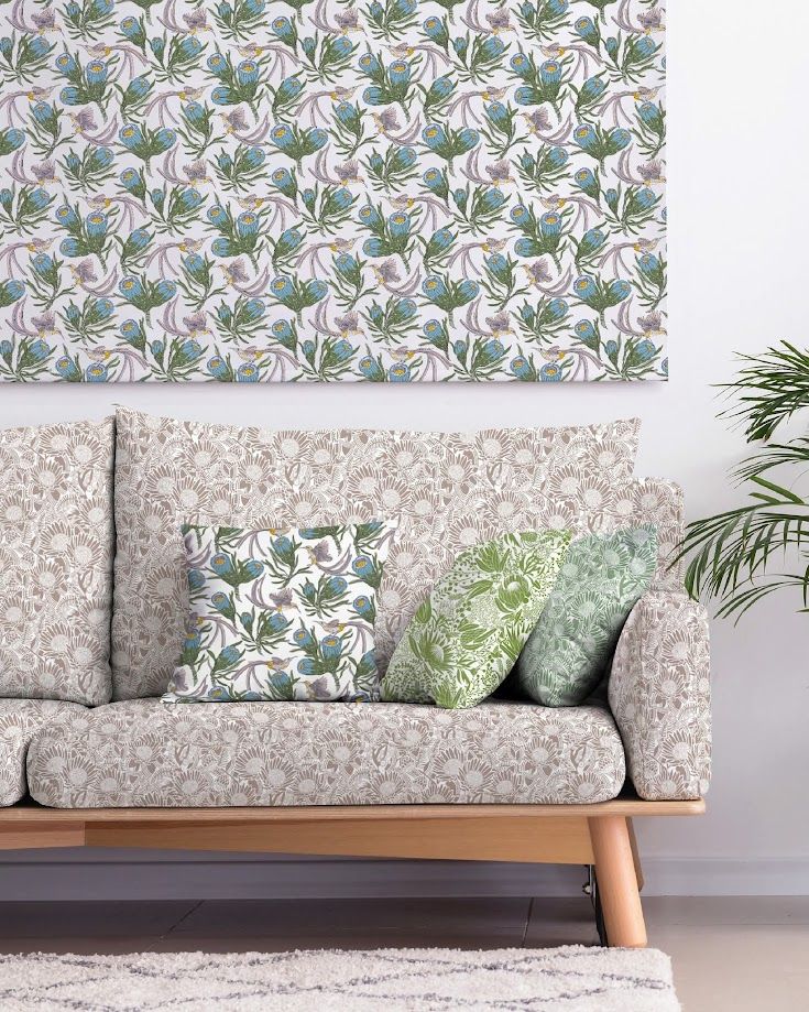 Floral patterned sofa with decorative pillows against matching wallpaper, with a green plant accent in a bright living room.