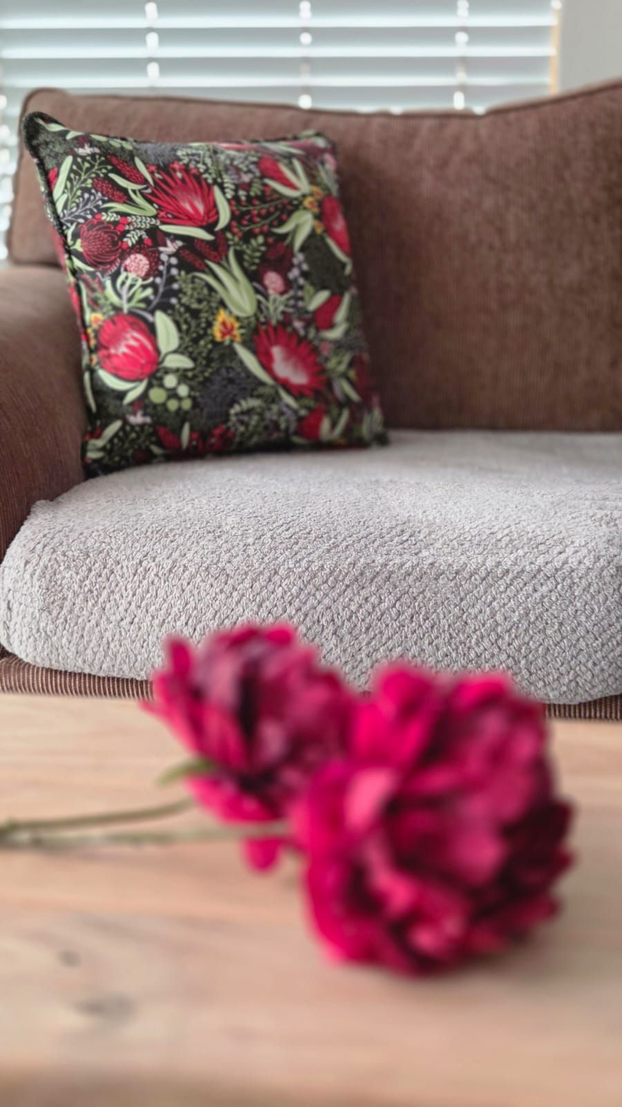 Cozy brown sofa with floral botanical cushion and vibrant pink peonies on wooden coffee table.