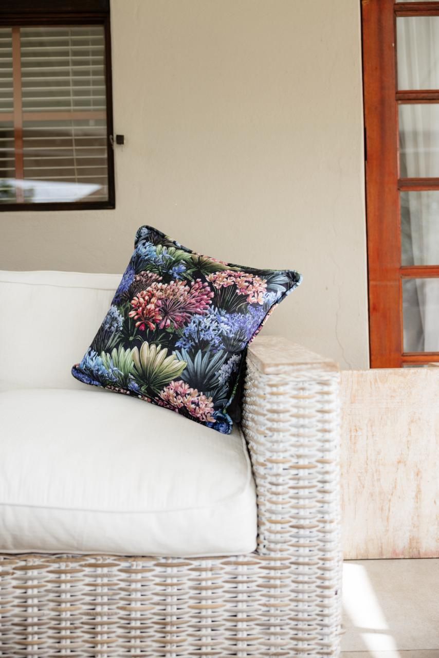 Floral patterned cushion on white wicker outdoor sofa on a patio near wooden framed windows.