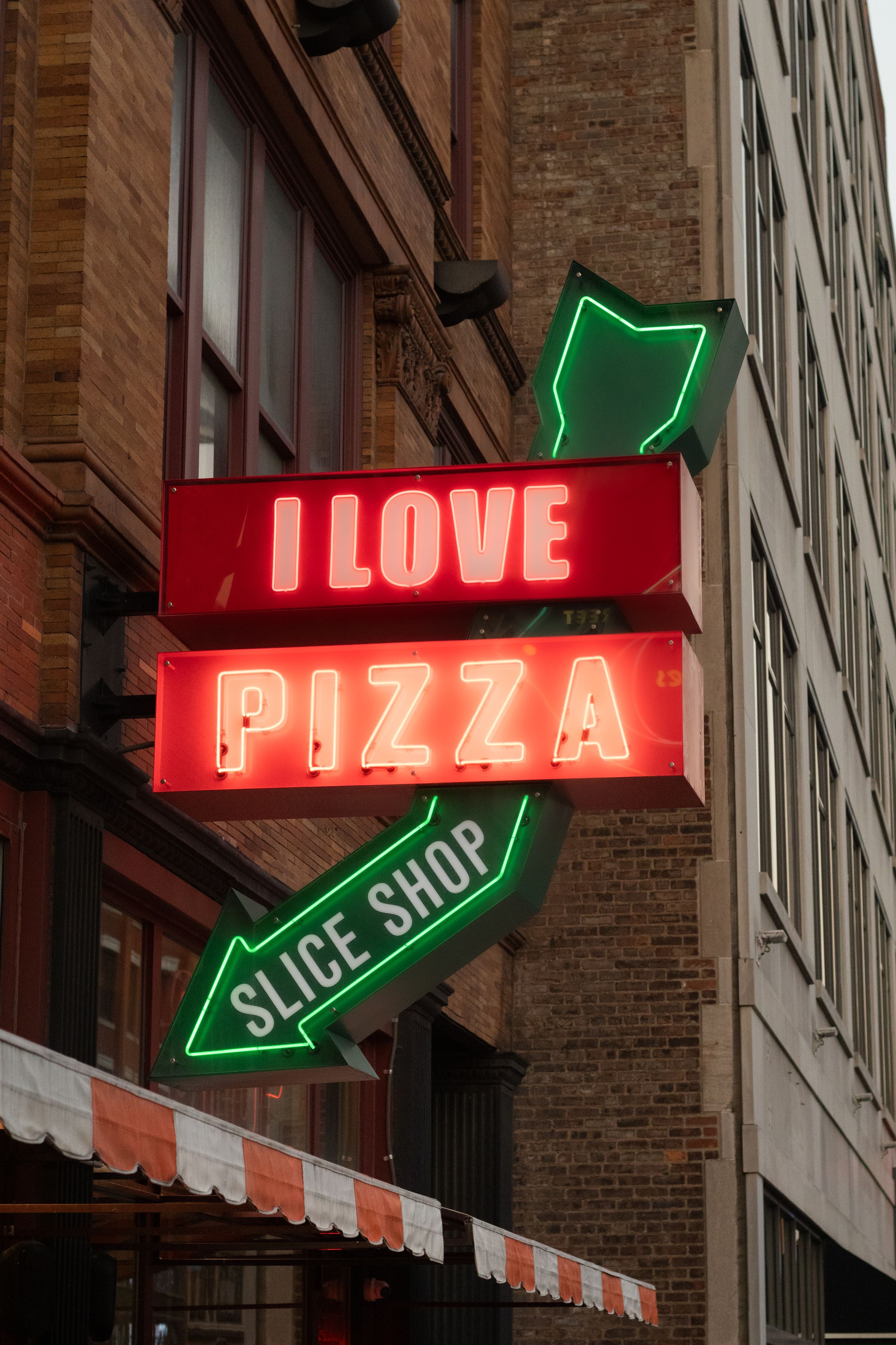 Bright neon sign reading I Love Pizza Slice Shop mounted on a brick building exterior.