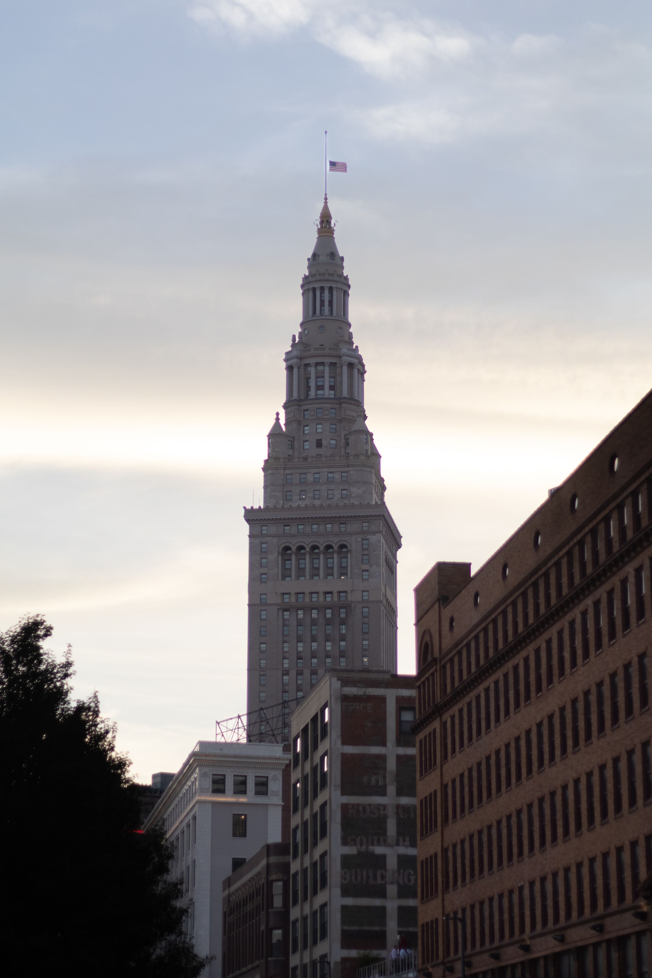 Terminal Tower skyscraper with American flag at dusk in Cleveland, Ohio skyline surrounded by historic buildings.
