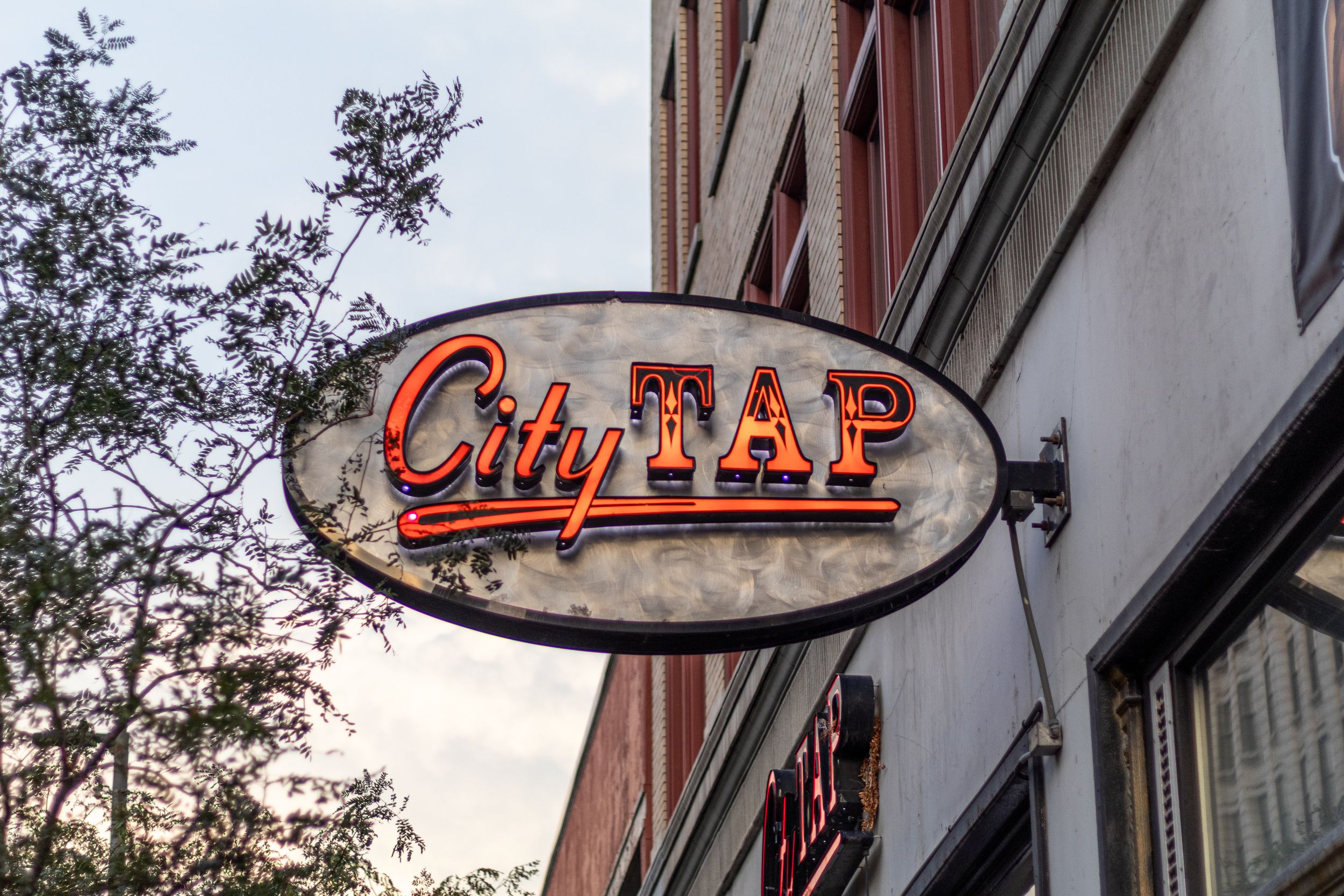 City Tap bar and restaurant oval neon sign mounted on brick building exterior wall.