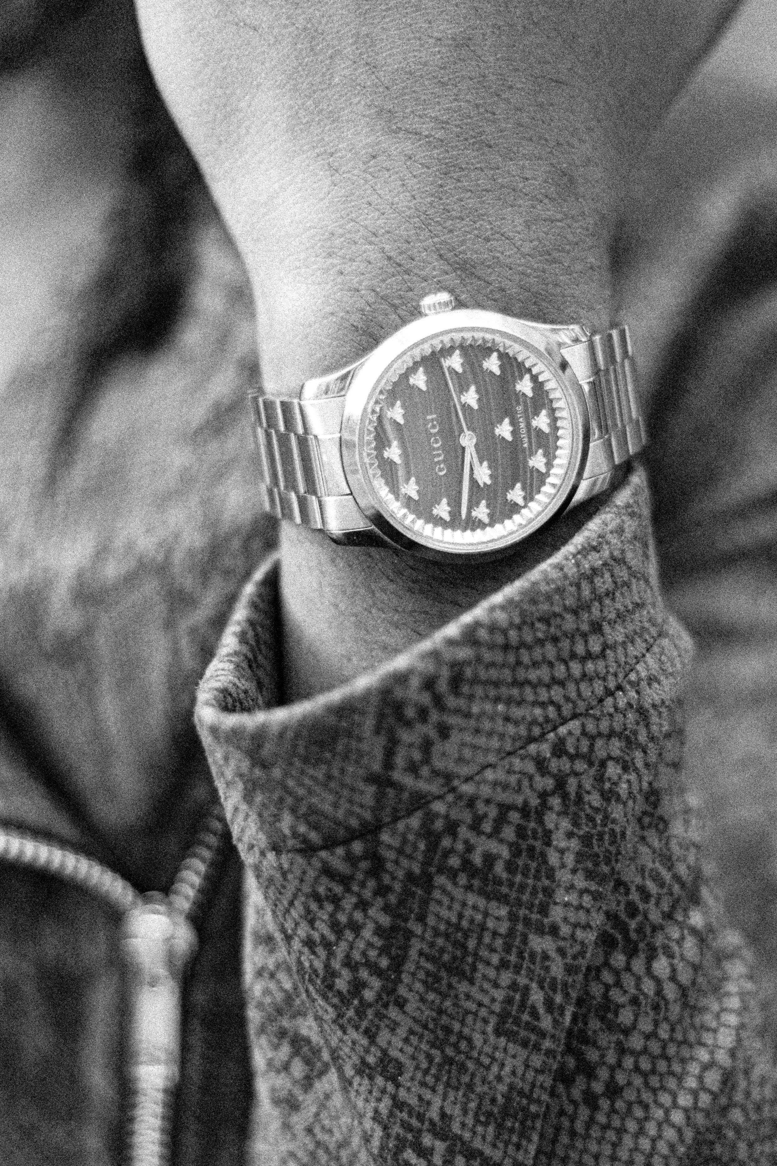 Close-up black and white photo of a wrist wearing a luxury steel watch with star-patterned dial on snakeskin jacket.