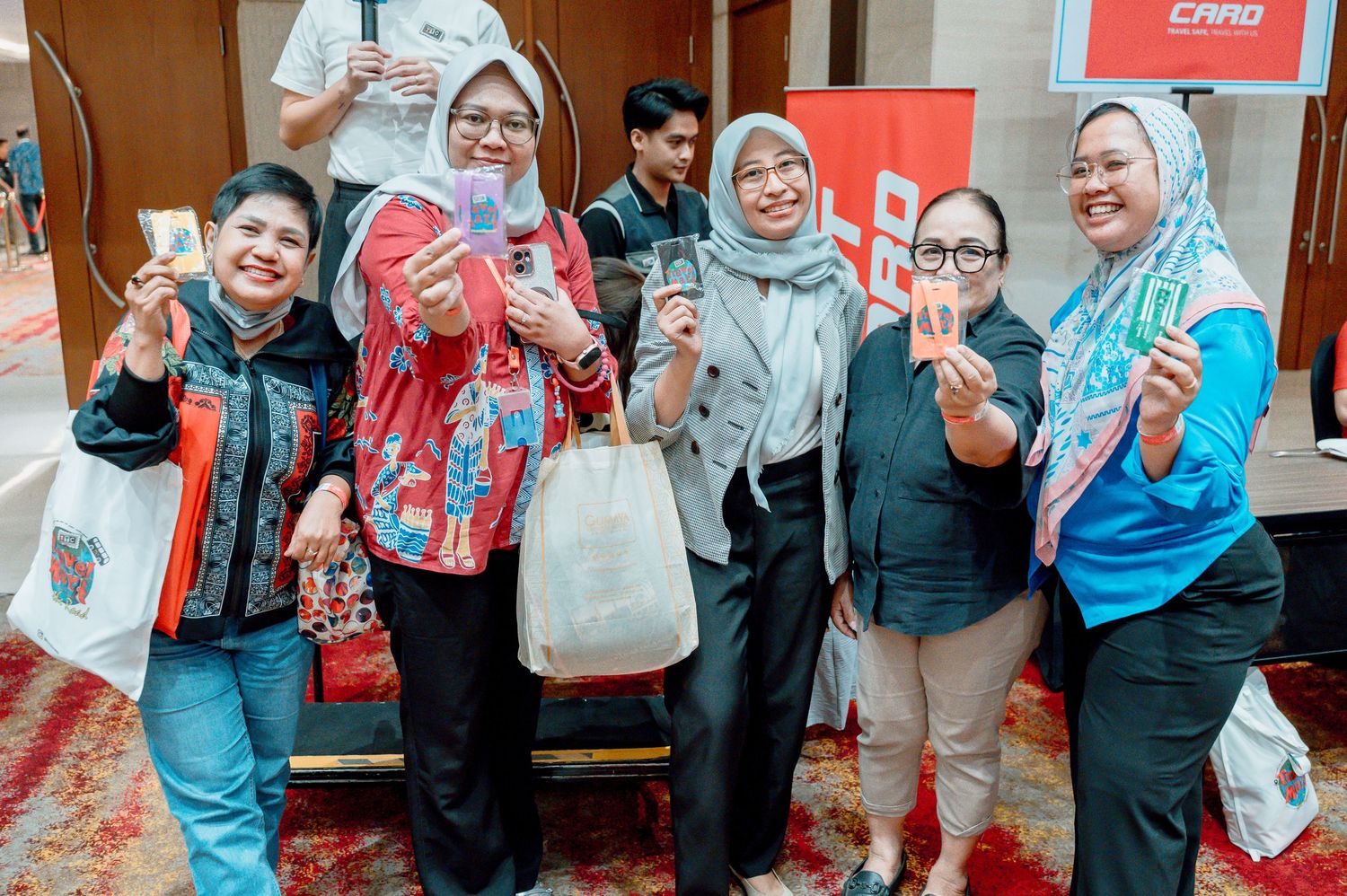 Group of five women in hijabs smiling and holding cards at a corporate event in Indonesia.