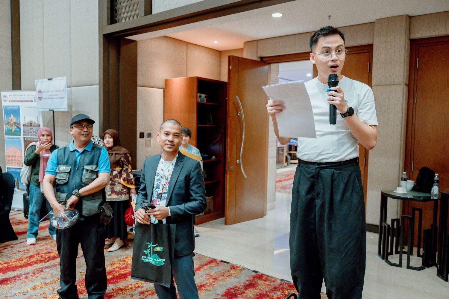 Business professionals speaking at a corporate event in a modern hotel conference room with attendees in background.
