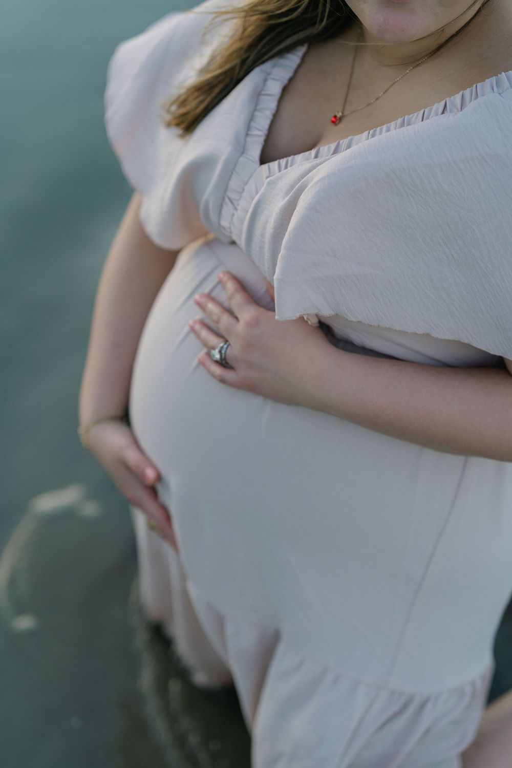 Close-up of an expectant mother cradling her belly during a beach maternity session.