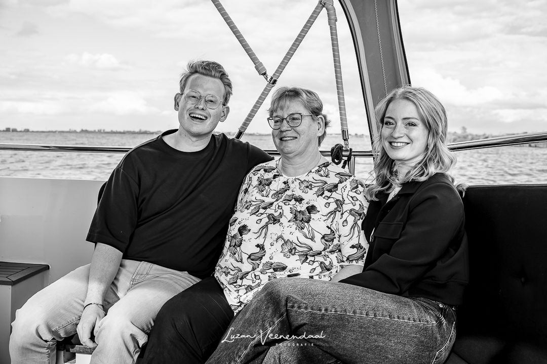 Moeder zit tussen zoon en dochter op de bank aan de achterzijde van de boot tijdens de familiefotoshoot in Uitgeest