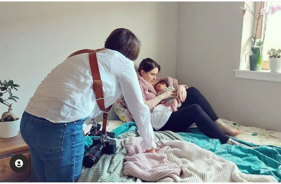 A newborn photography session setup in progress with camera equipment and soft lighting on a bed.