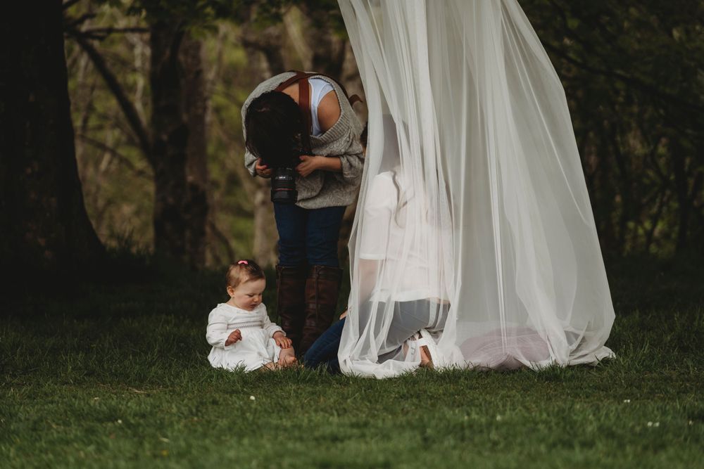 Intimate wedding photo session featuring flowing white dress and small child on grass.