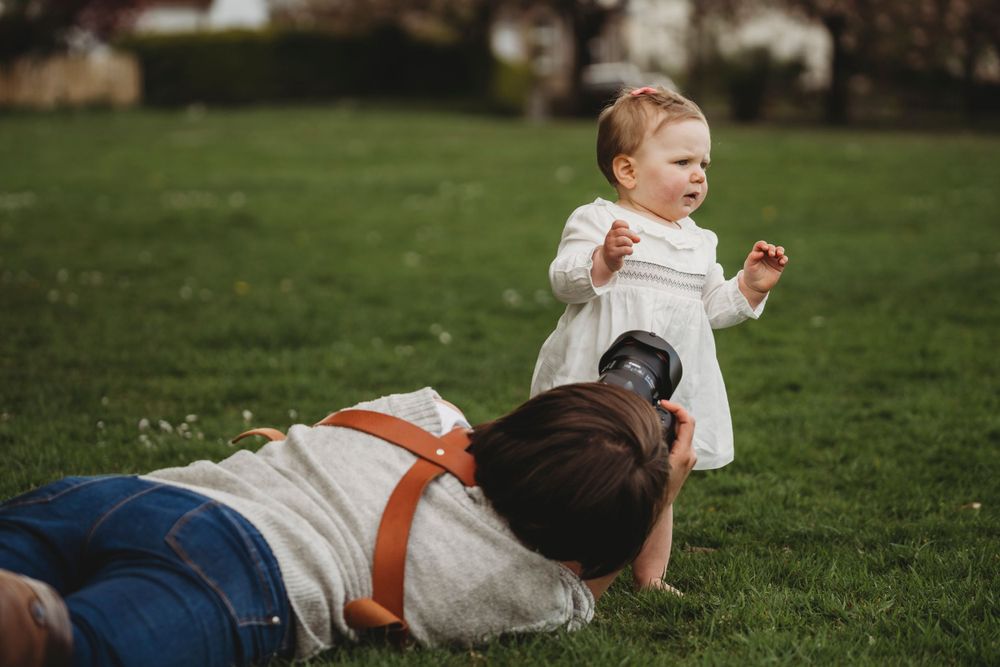 Playful interaction between parent and toddler on green grass during outdoor photoshoot.
