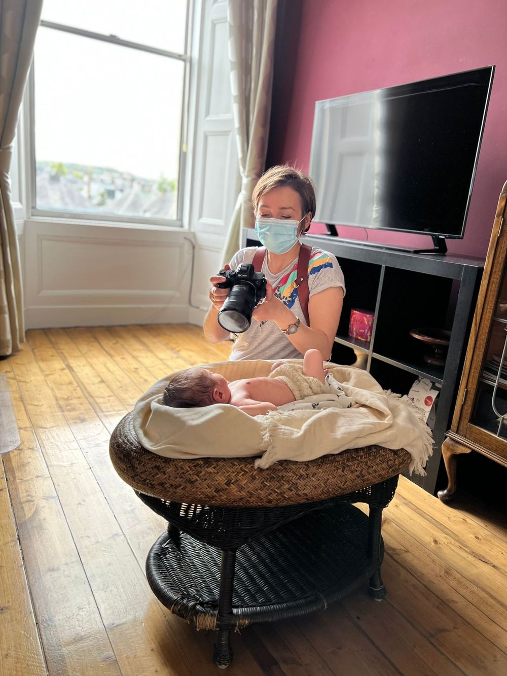 A photographer reviews images on their camera while working in a bright room with hardwood floors.