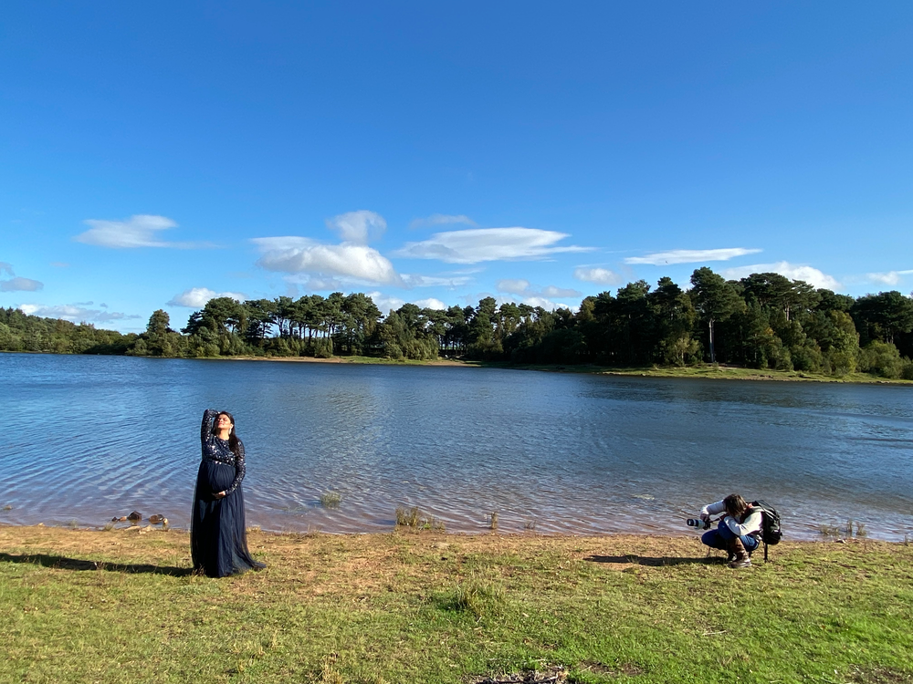 Photographers capturing shots by a serene lake with blue skies and tree-lined shore.