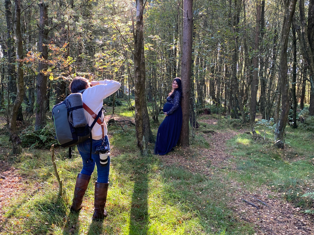 A photographer captures shots of a subject in a blue dress along a mossy forest trail.