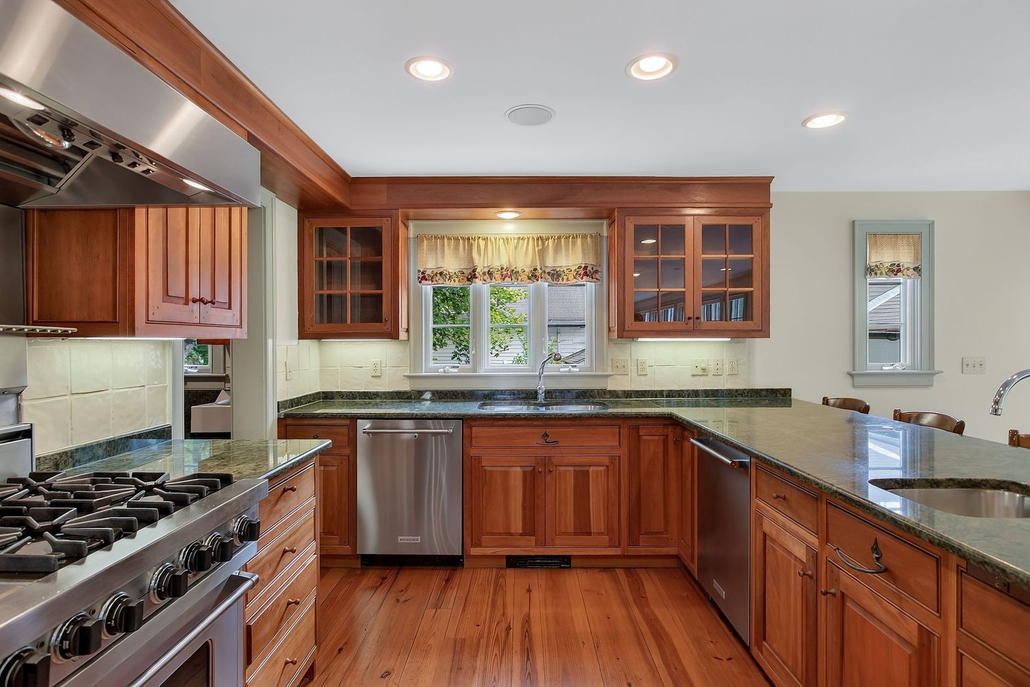 Warm cherry wood kitchen with granite counters, stainless appliances, and hardwood floors.