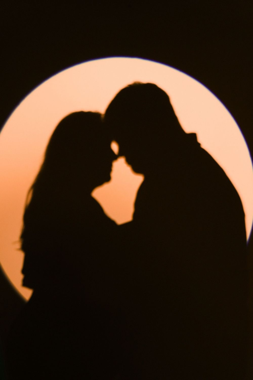 Romantic silhouette of a couple about to kiss framed by a glowing circular light against a dark background.