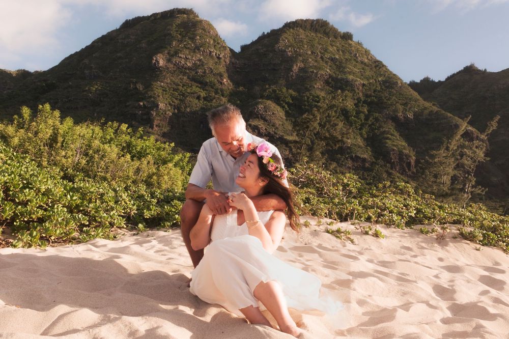Couple sitting together on a quiet North Shore Oahu beach beneath tropical mountains