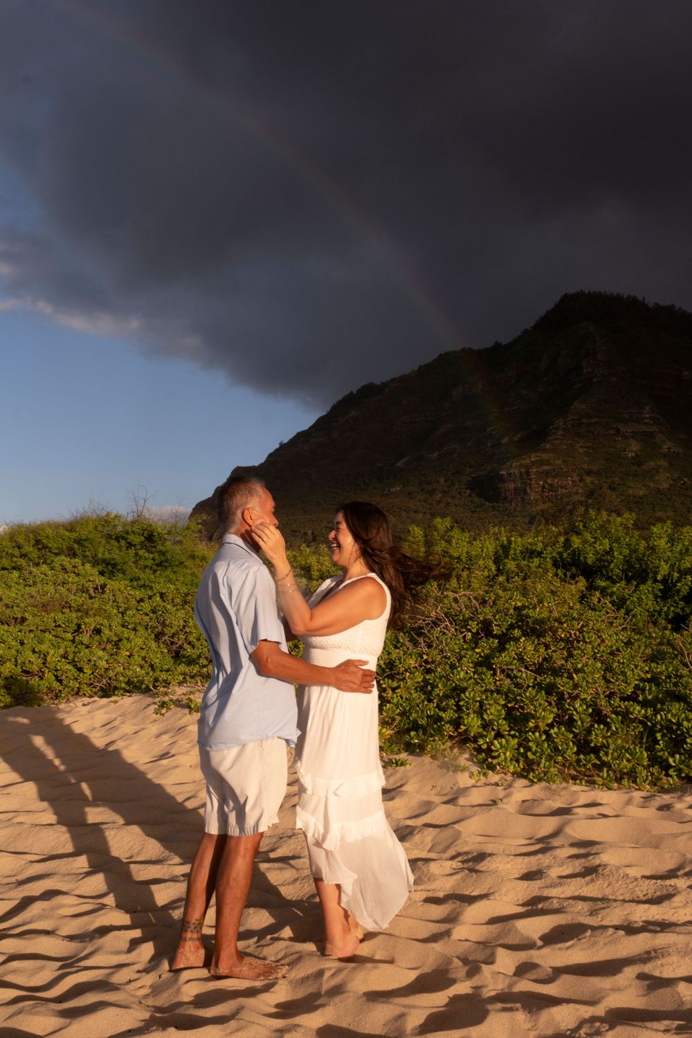 Couple sharing a quiet moment on the sand under the rainbow during a North Shore Oahu photography session
