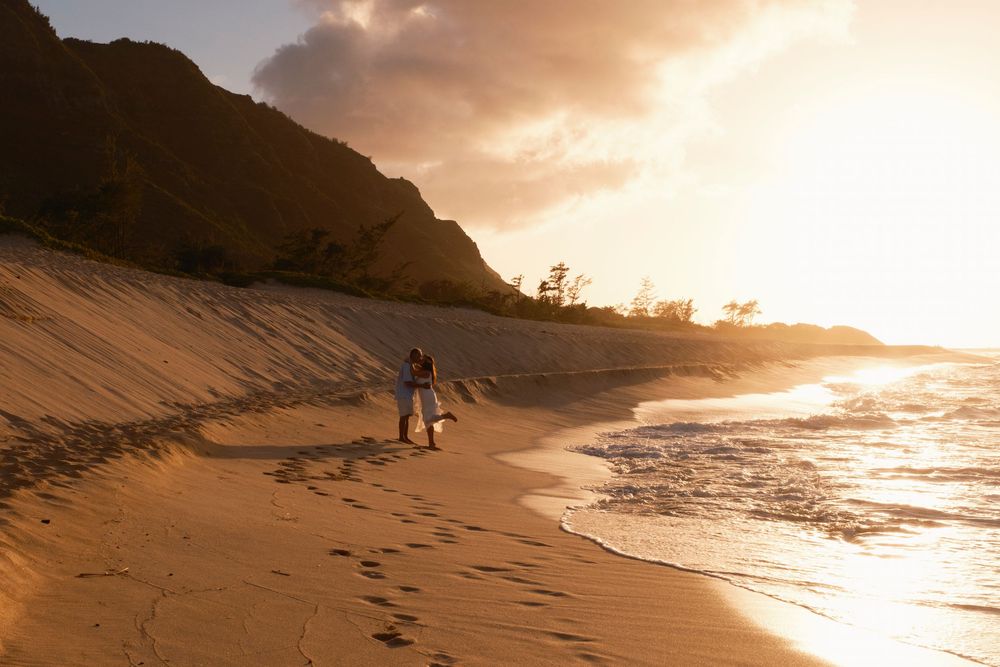 Couple walking along a secluded North Shore Oahu beach at golden hour.