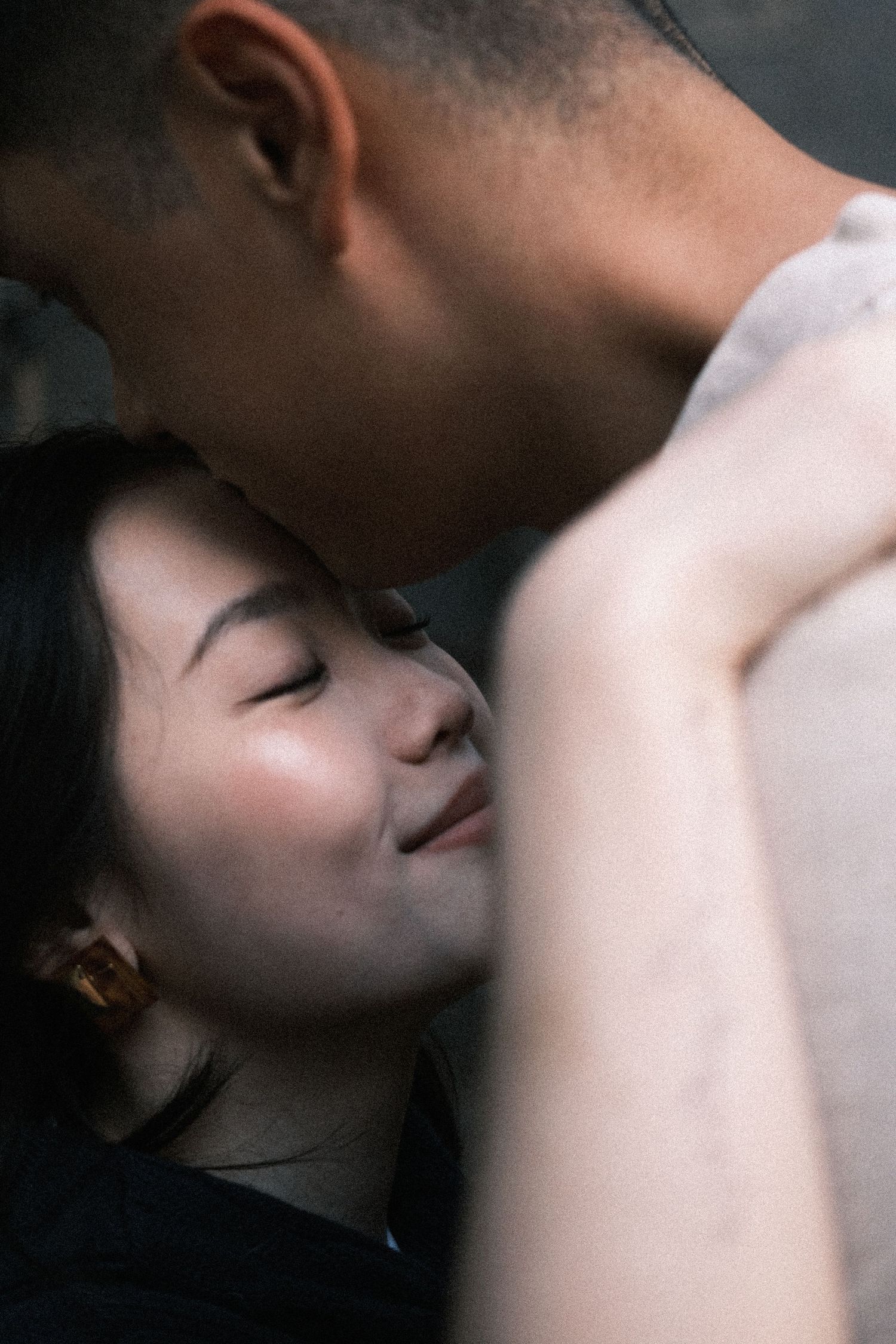 Intimate couple sharing a tender moment, woman with closed eyes smiling softly against man's chest.