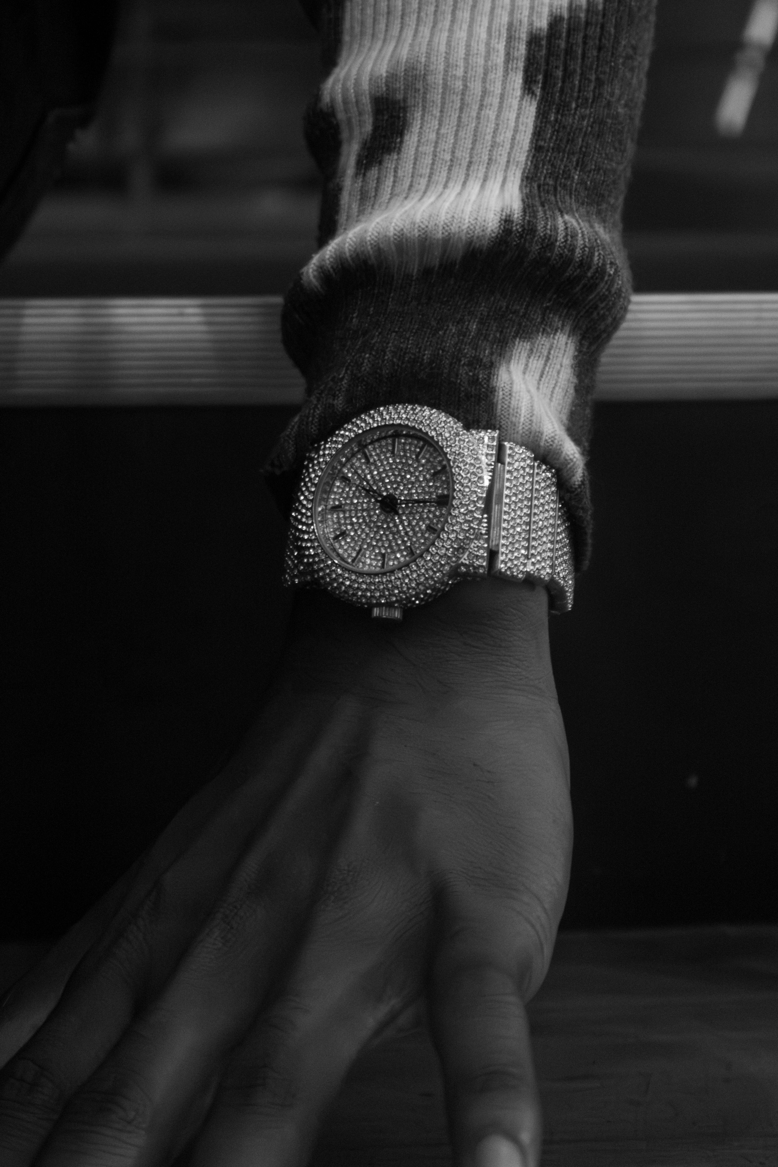 Black and white photo of a hand wearing a diamond-encrusted luxury watch with a sparkling bracelet band.