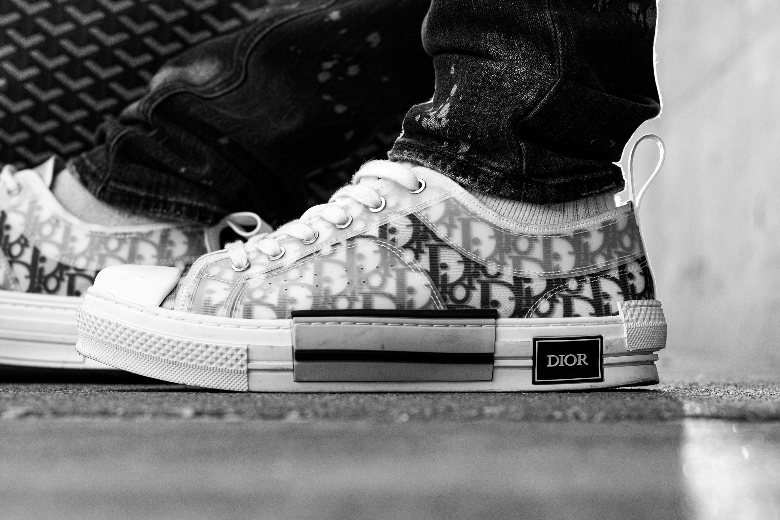 Black and white close-up of Dior Oblique sneakers worn on feet, showcasing luxury streetwear fashion.