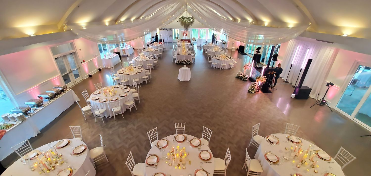 Elegant wedding reception hall with round tables, white chairs, floral centerpieces, and soft pink ambient lighting.