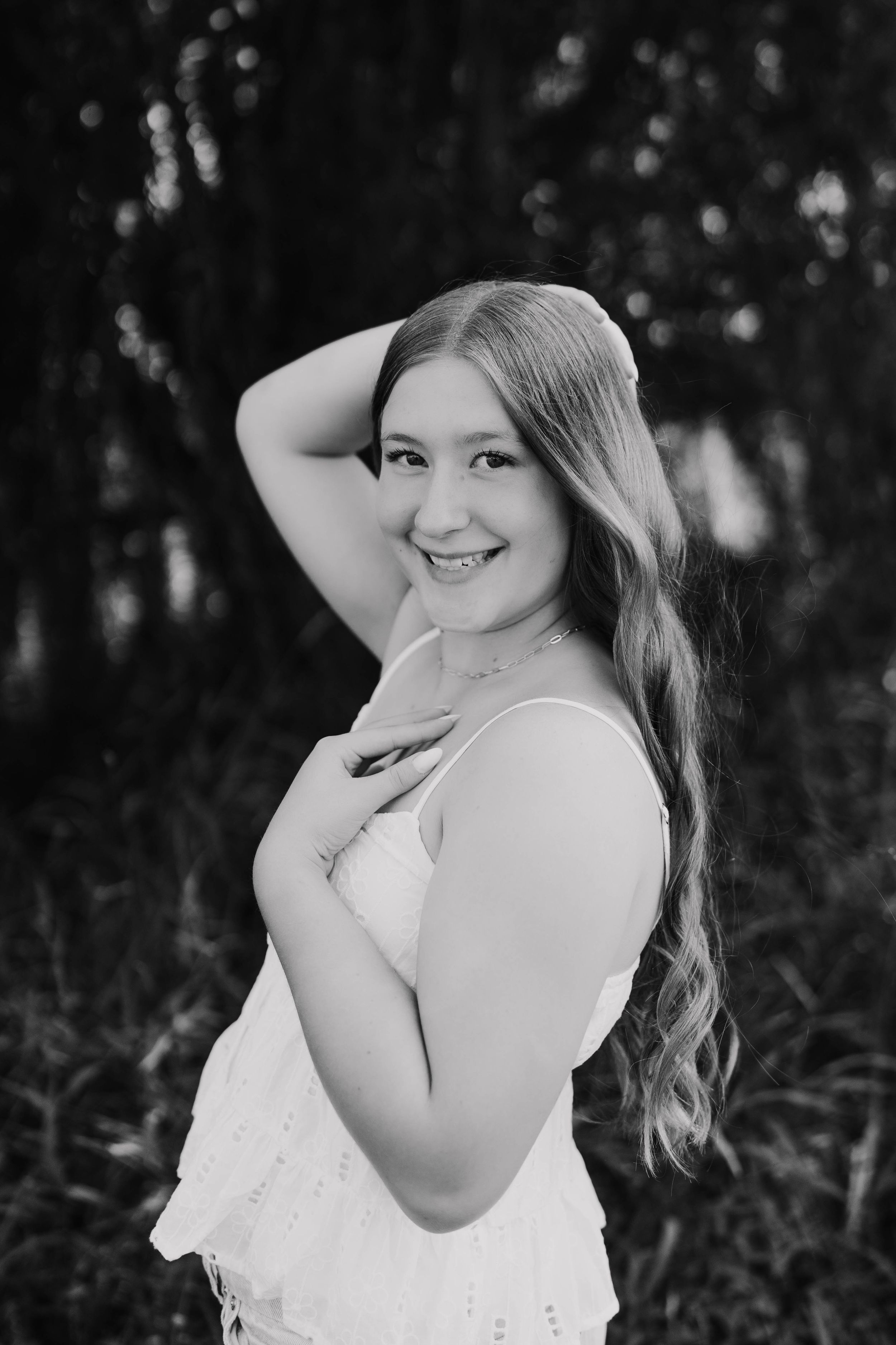 Black and white portrait of a smiling young woman with long hair in a white dress posing outdoors.
