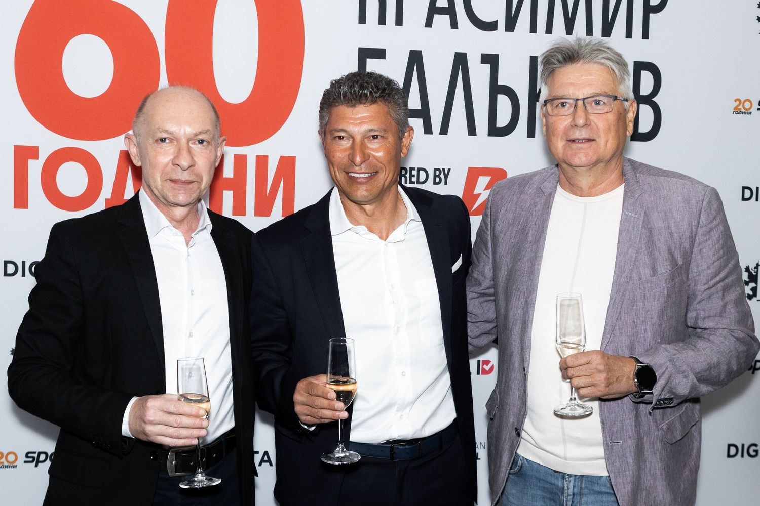 Three men in suits holding champagne glasses pose together at a formal event with Cyrillic text backdrop.