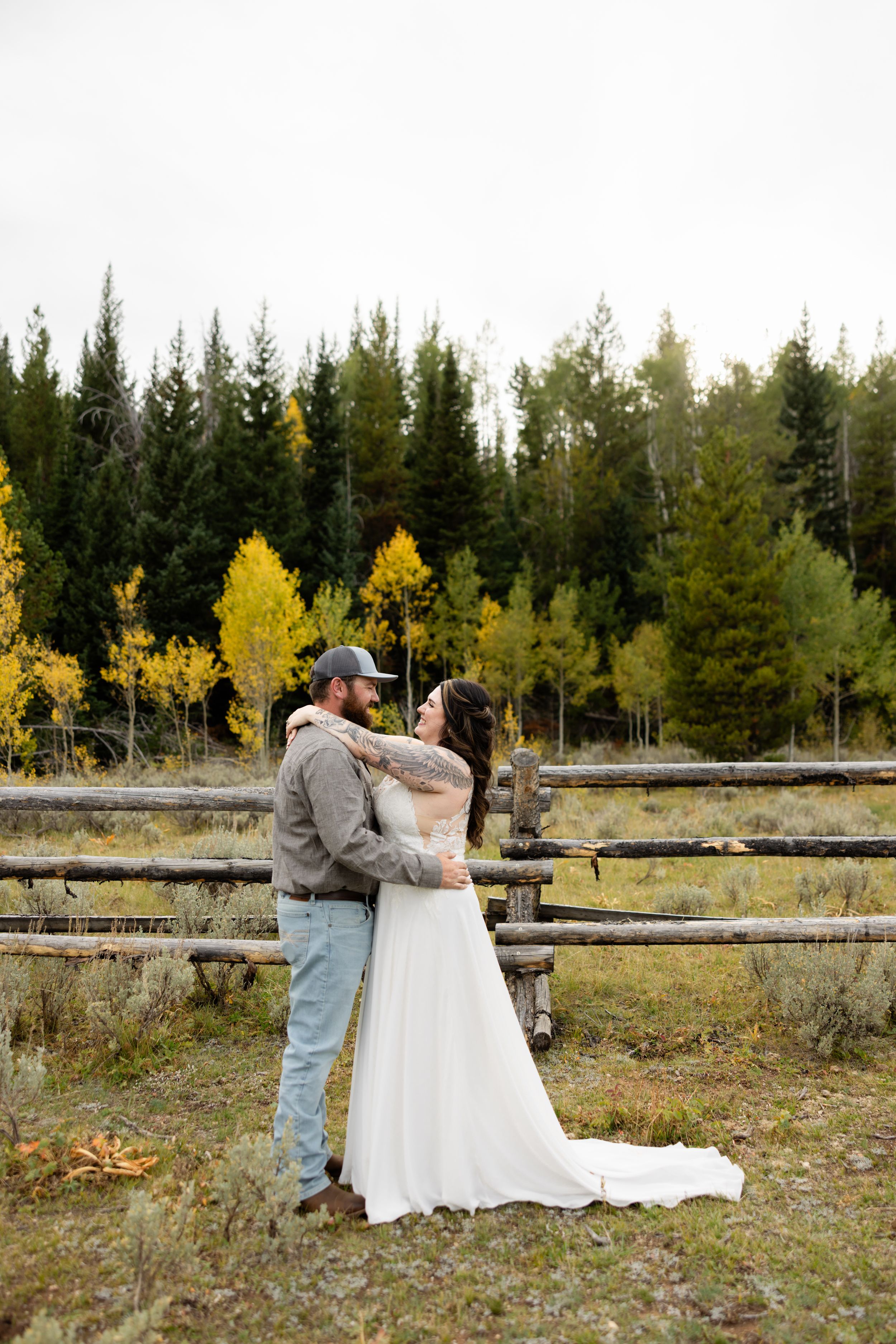 Bride and groom share romantic moment by wooden fence surrounded by colorful autumn forest during outdoor wedding.