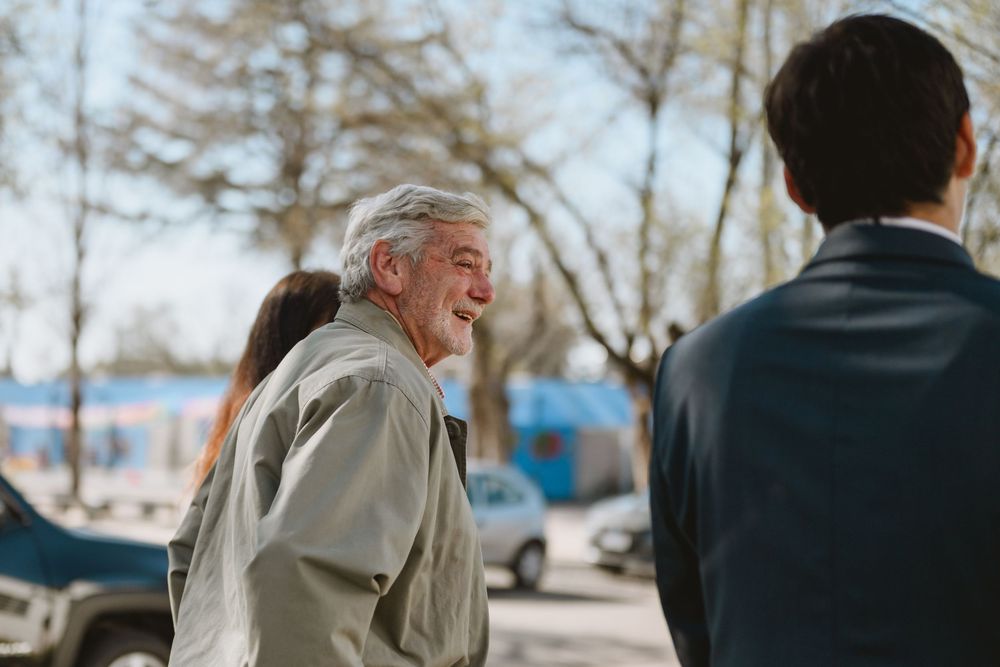 Elderly man with white hair laughing joyfully outdoors at a wedding celebration.