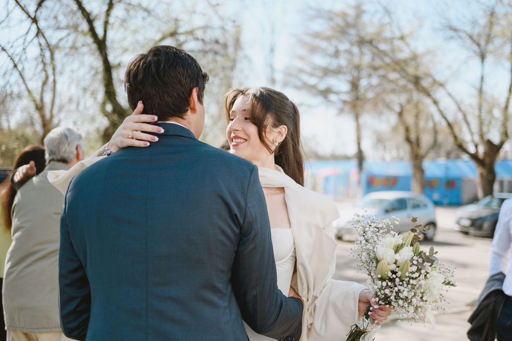 Bride smiling and embracing guests outdoors while holding a delicate white floral bouquet.