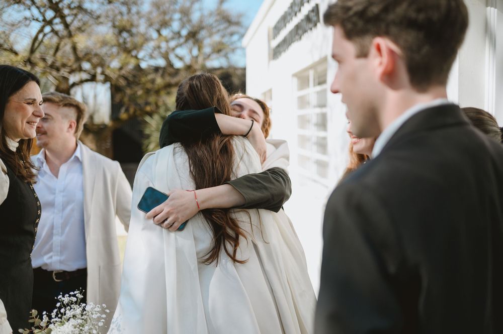 Bride in white wedding dress embracing a guest warmly outside wedding venue.