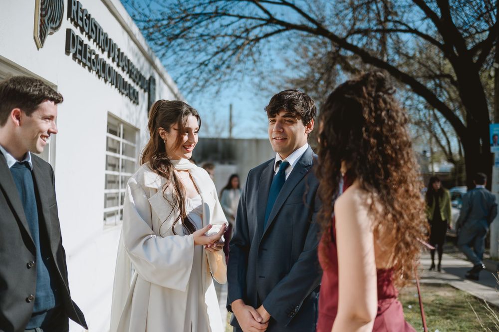 Wedding couple in formal attire greet guests outside a registry office on a bright sunny day.