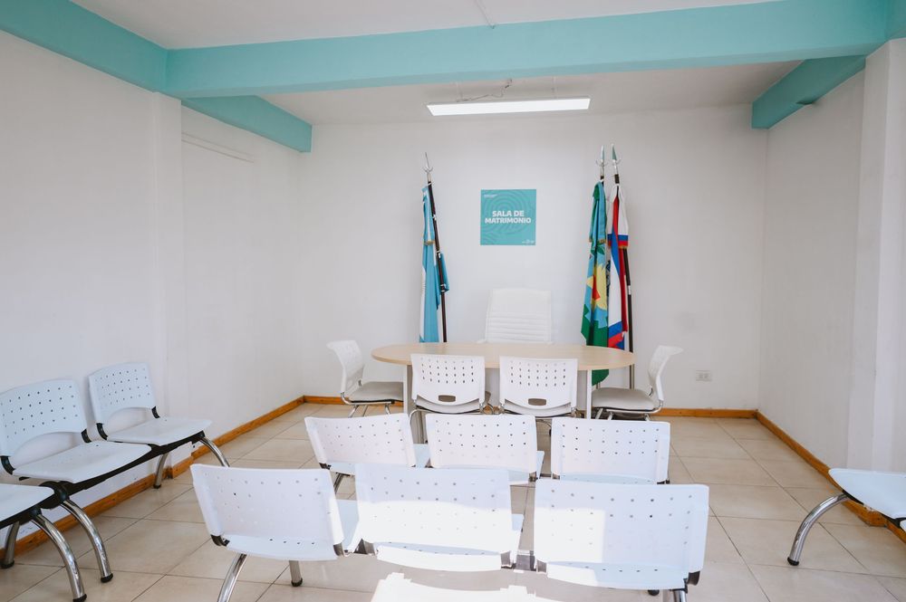 Small civil ceremony room with white chairs, flags, and a registration desk with teal accent decor.