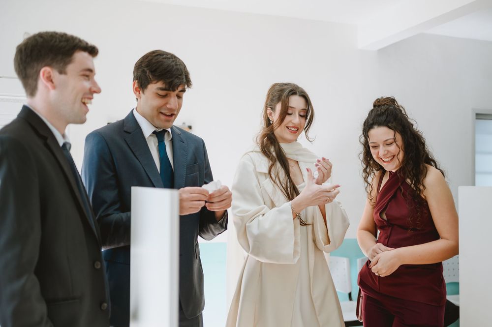 Four elegantly dressed young adults smiling and chatting at a formal event indoors.