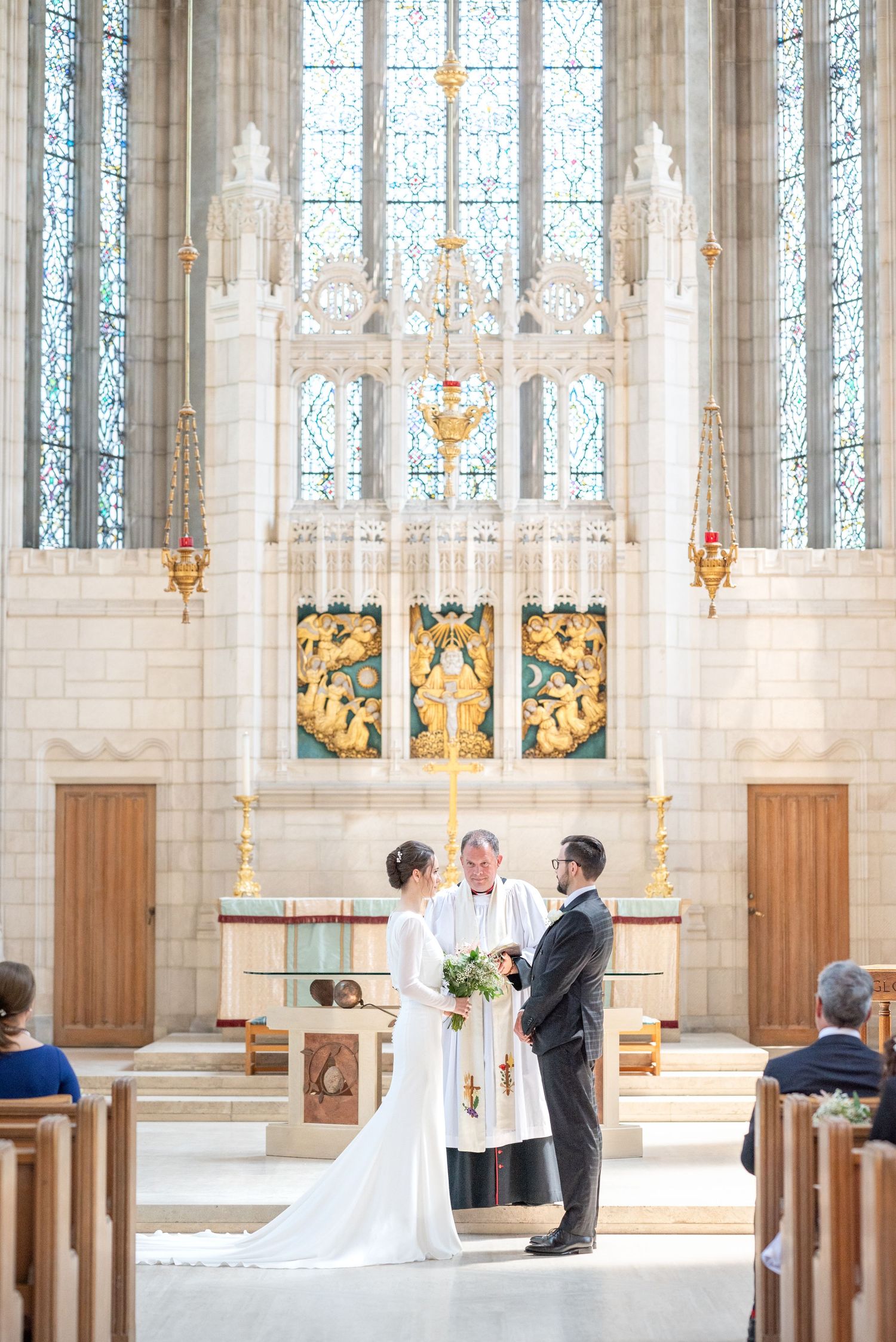 Bride and groom exchange vows at ornate church altar with stained glass windows and golden accents during wedding ceremony.