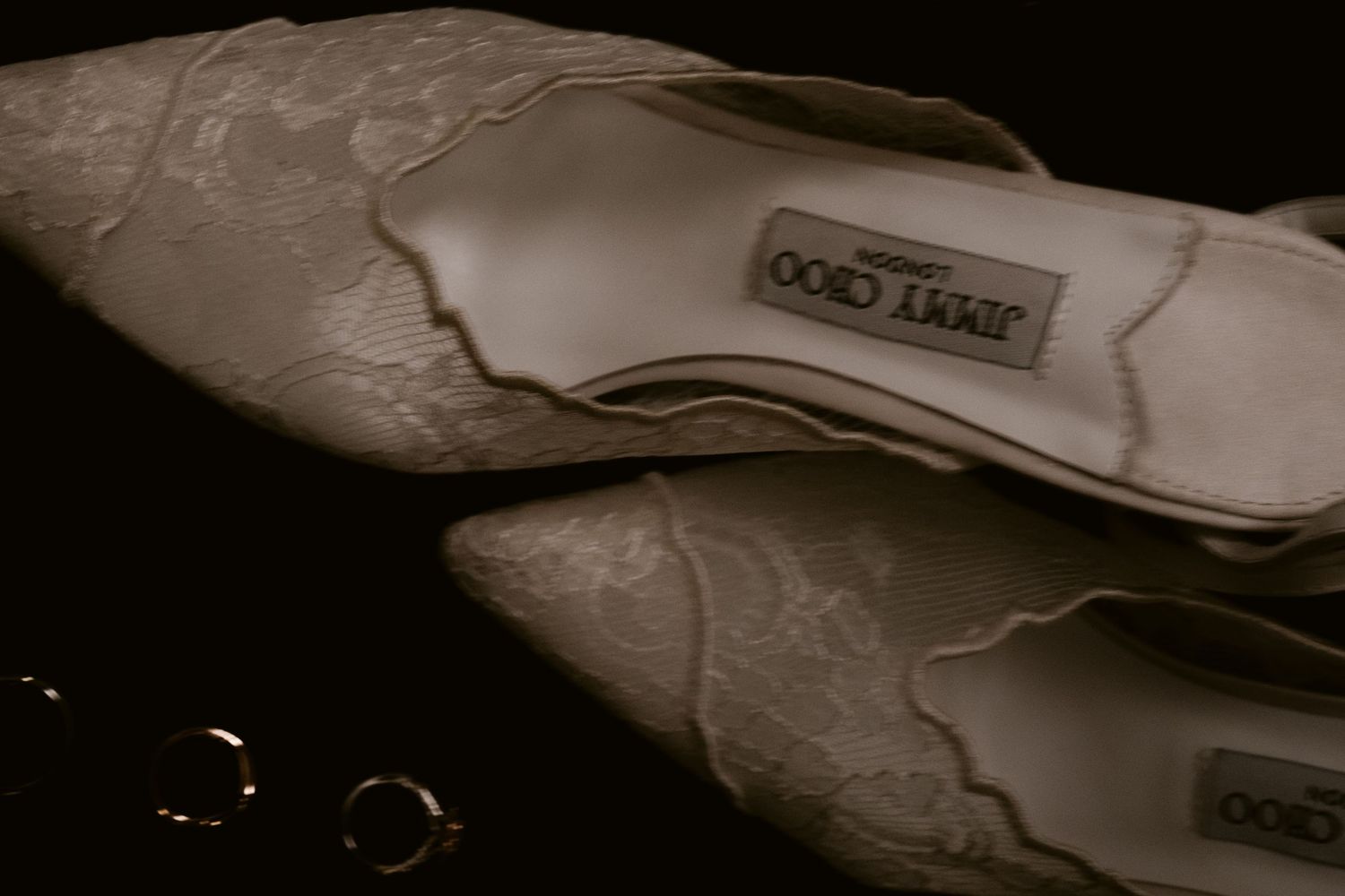 Close-up of ivory Jimmy Choo lace bridal heels with delicate floral detail on dark background.