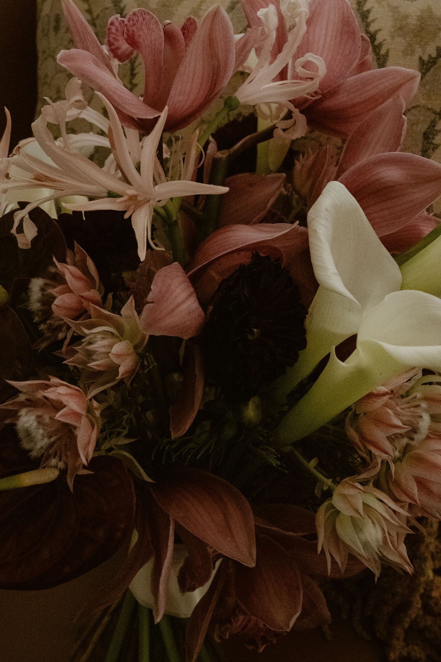Close-up of lush bridal bouquet with burgundy orchids, calla lilies, and dried flowers.