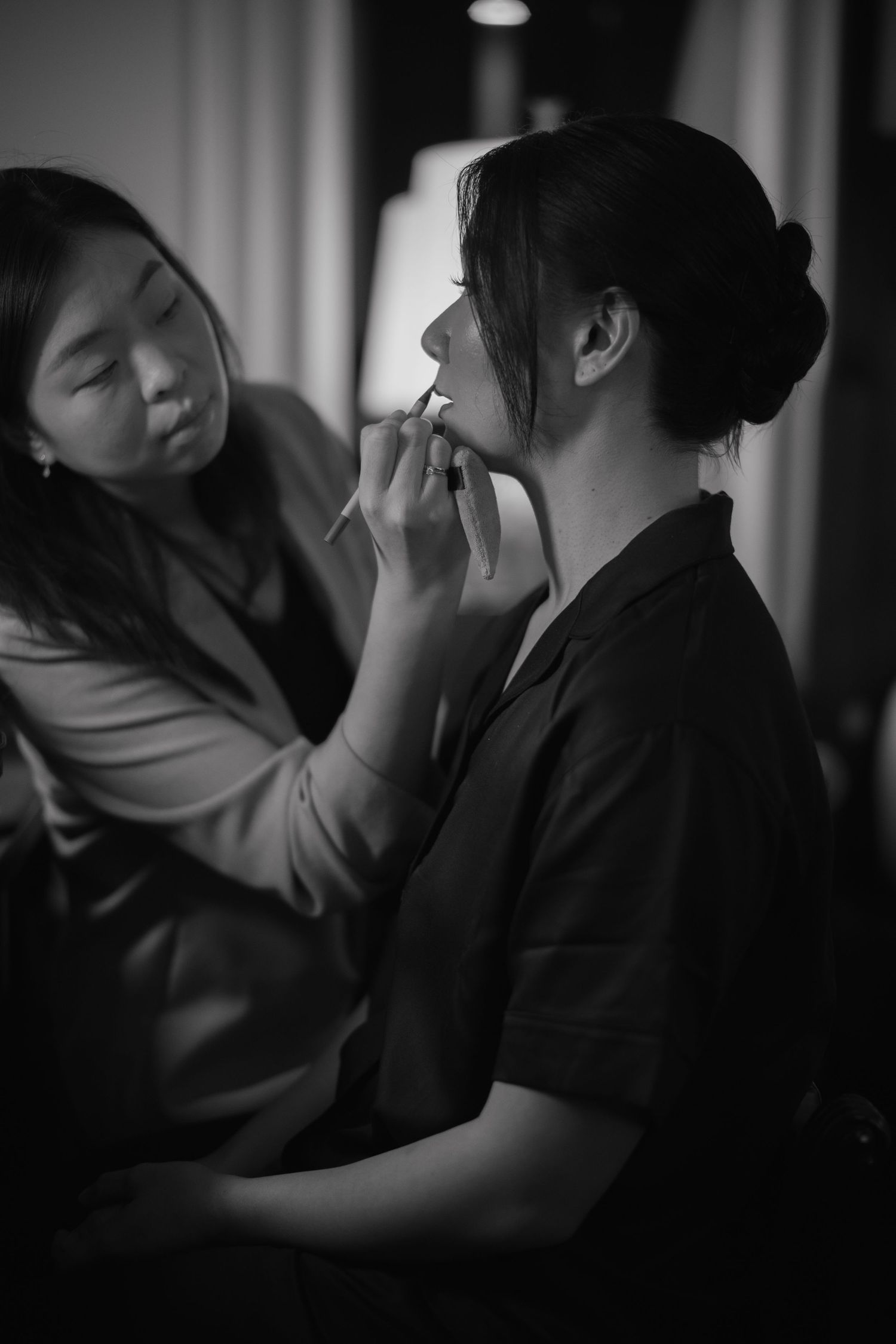 Makeup artist applying lipstick to a bride in black and white photo.