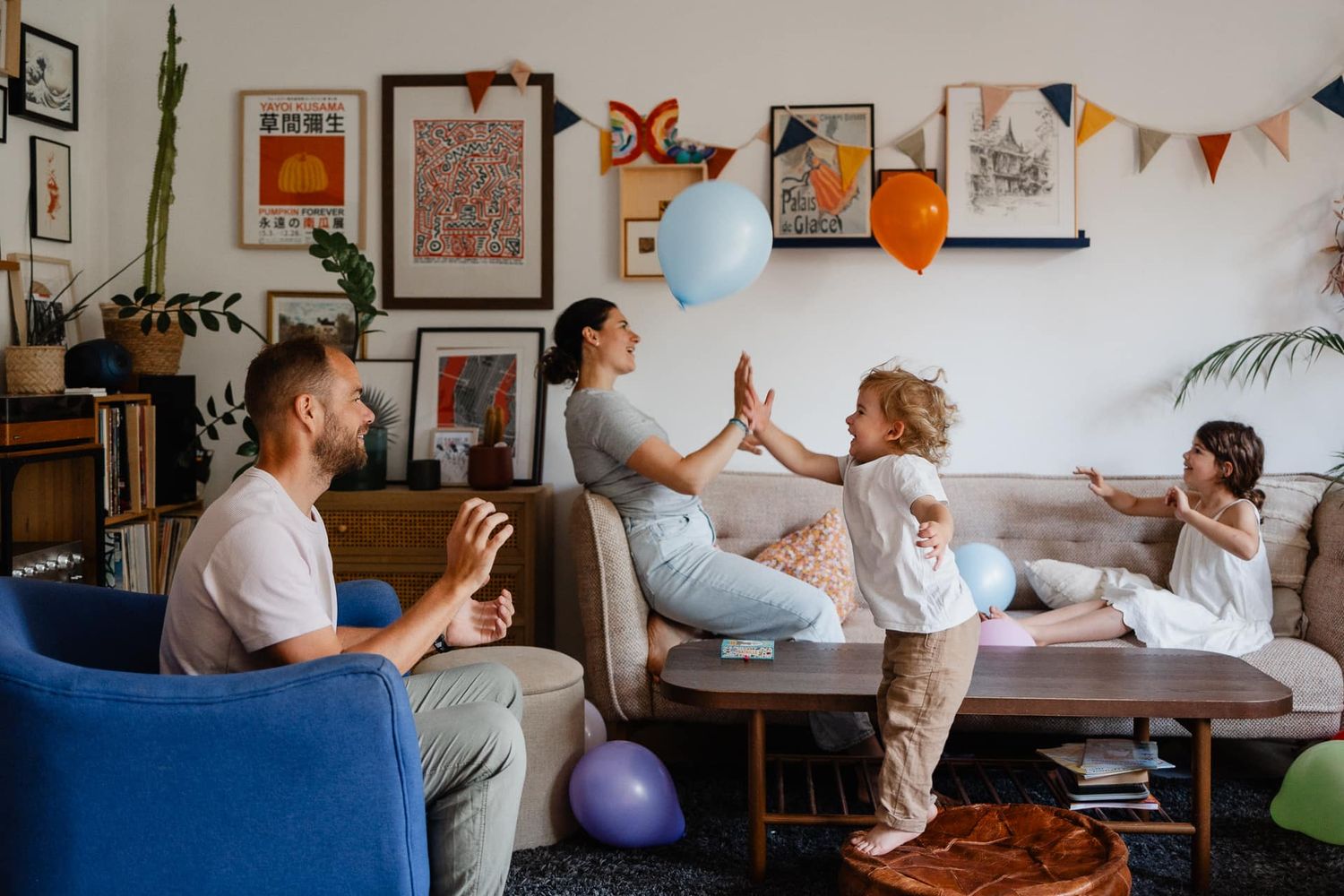 Photographe famille a domicile a Lille, tout-petit qui saute sur un pouf pour taper dans un ballon et l'envoyer a son papa