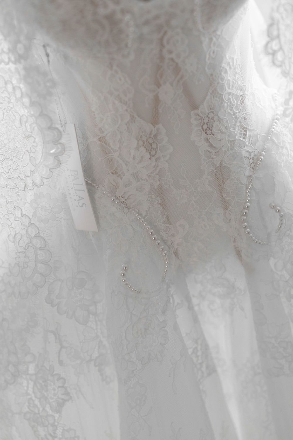 Close-up of elegant white lace wedding dress with delicate pearl jewelry and floral lace pattern detailing.