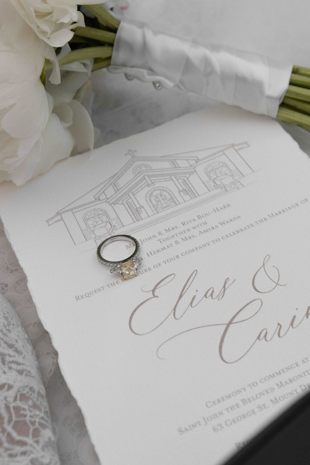 Elegant wedding invitation for Elias and Cari with diamond engagement ring, white peonies, and church illustration.