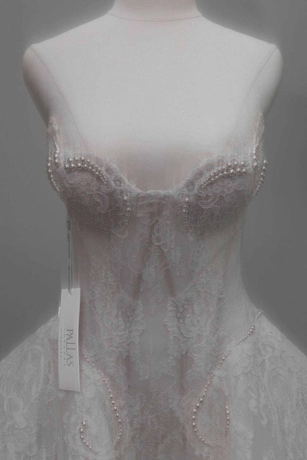 Pallas bridal gown on mannequin featuring strapless lace bodice with pearl embellishments and sheer overlay.