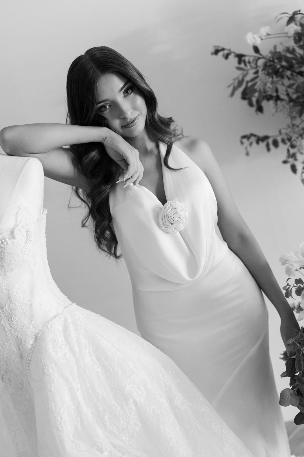 Elegant bride in a sleek white gown with a floral detail, posing gracefully in a black and white bridal portrait.