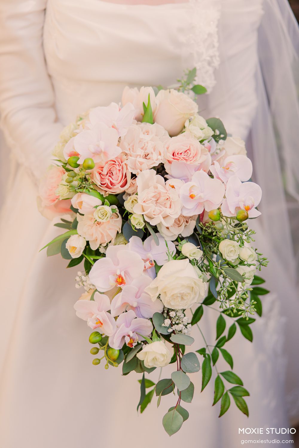 Bride holding cascading wedding bouquet with pink orchids, roses, and eucalyptus greenery.
