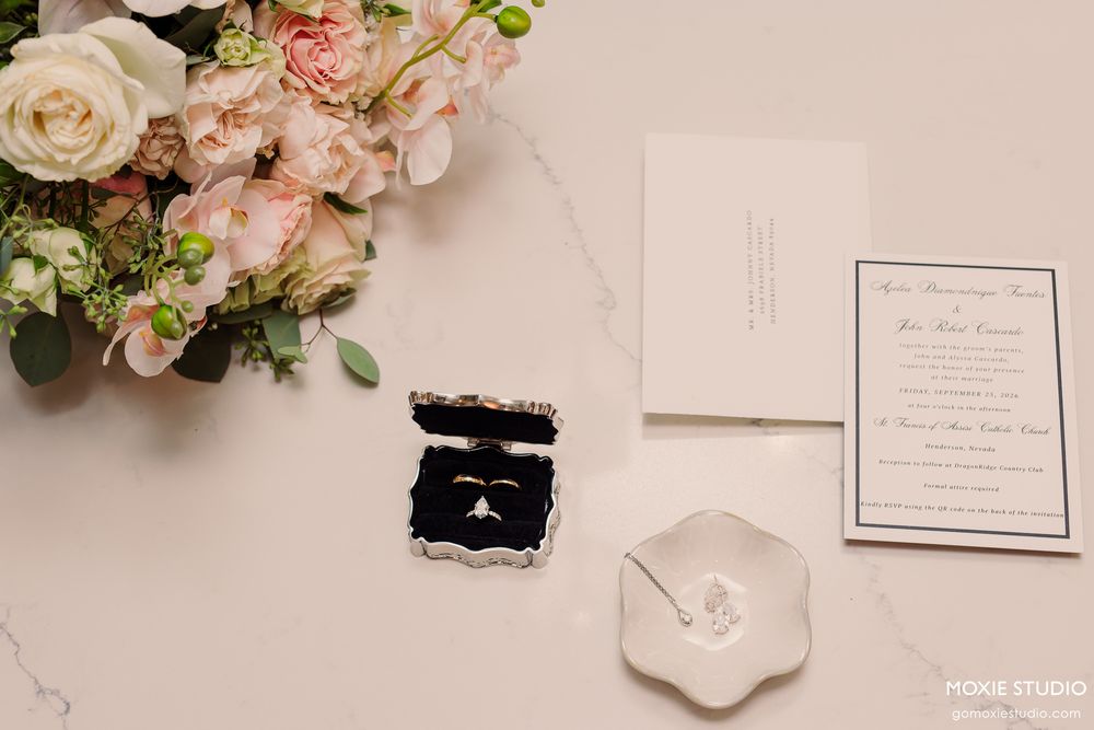 Wedding rings in velvet box beside floral bouquet and invitation suite.