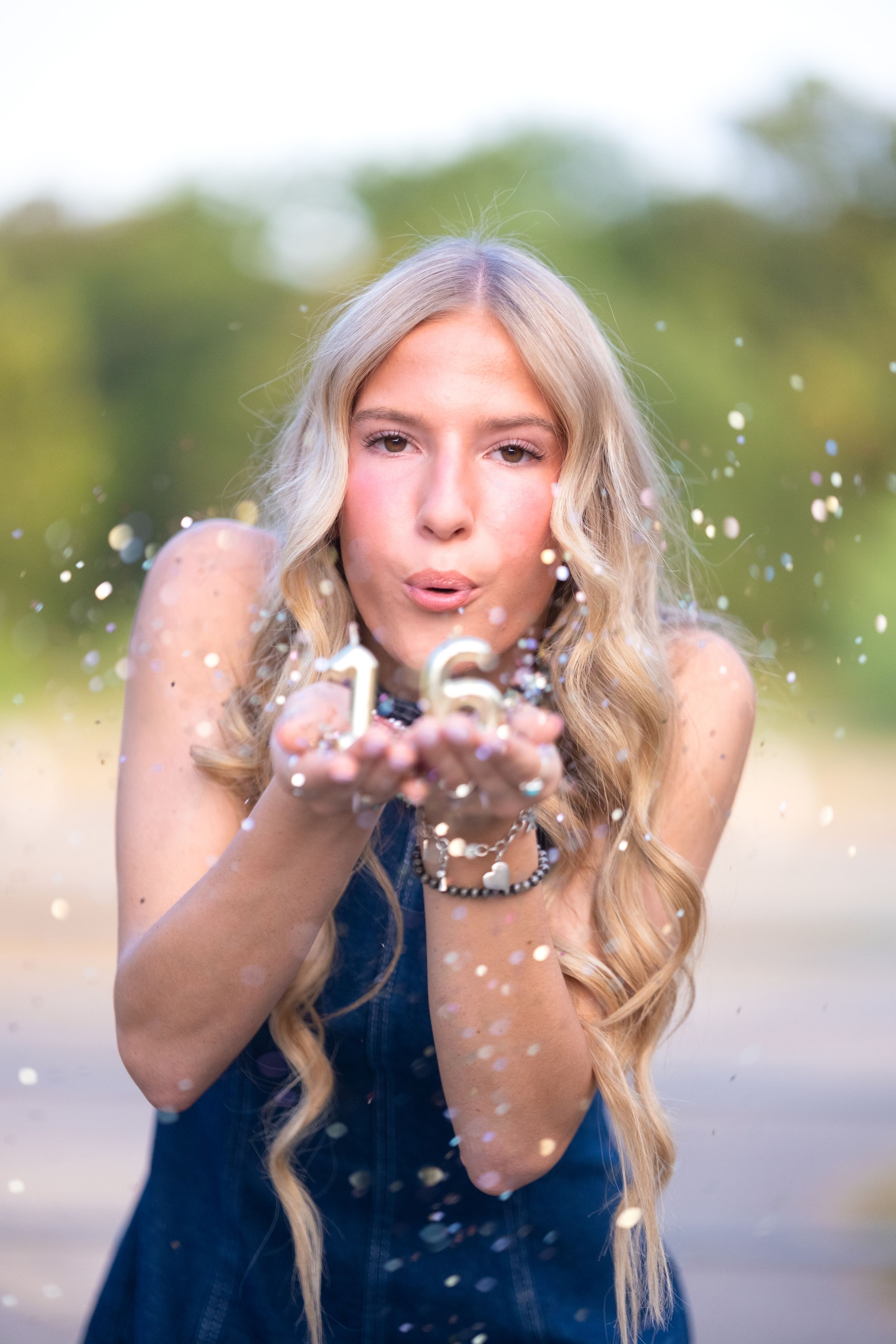 Blonde teen blowing glittery number 16 confetti from her hands in an outdoor birthday photo in Salado Creek, Salado Texas